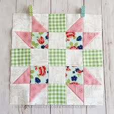 a pink and green patchwork quilt hanging on a white wooden wall next to scissors