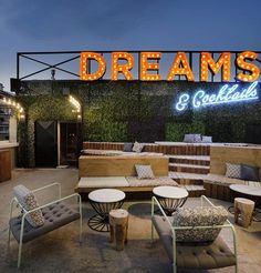 an outdoor seating area with couches, tables and chairs under a neon sign that reads dreams & cocktails