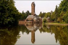 a large clock tower towering over a lake in front of a forest filled with trees