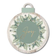 a round wooden ornament with the word joy in gold lettering and evergreen leaves