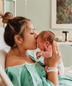 a woman holding a baby in her arms and kissing it's face with the other hand