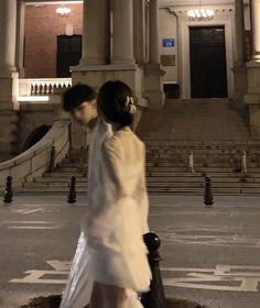 a man and woman walking down the street in front of an old building at night