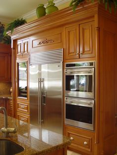 a stainless steel refrigerator and oven in a kitchen with wooden cabinets, granite counter tops and an island