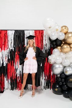 a woman standing in front of balloons and streamers with a graduation cap on her head