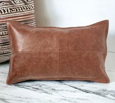 a brown leather pillow sitting on top of a white marble counter next to a decorative pillow