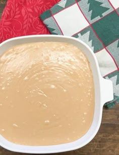 a white bowl filled with batter sitting on top of a wooden table next to a red and green towel