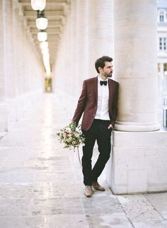 a man in a tuxedo leaning against a column