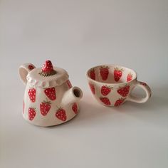 two cups and a teapot with strawberries painted on them are sitting next to each other