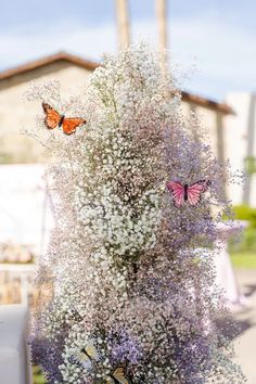 two butterflies are sitting on the flowers in front of a building and another butterfly is flying around