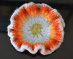 an orange and white crocheted flower on a black surface