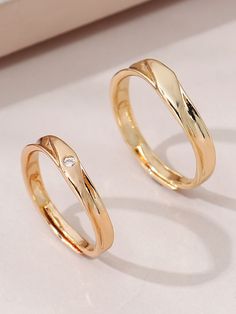 two gold wedding rings sitting next to each other on a white surface with a diamond in the middle