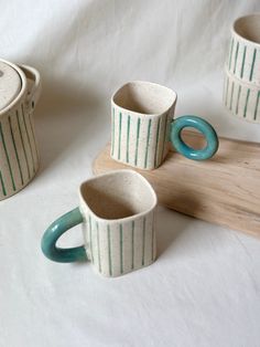 three ceramic mugs sitting next to each other on a wooden board and white background