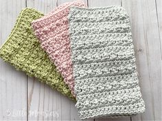 three crocheted dishcloths sitting on top of a white wooden table next to each other