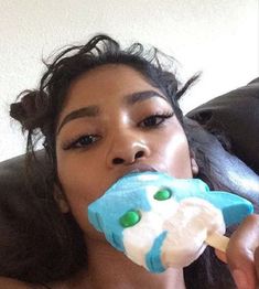 a woman laying on top of a black couch eating an ice cream cone in her mouth