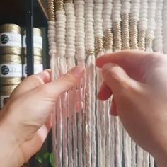 two hands are working on a beaded wall hanging from a shelf in front of other beads