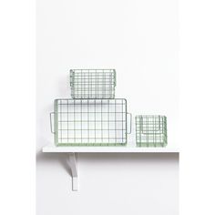 three green wire baskets sitting on top of a white shelf next to each other in front of a white wall