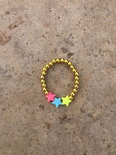 This bracelet is a gold beaded bracelet with plastic colorful stars Trendy Star Shaped Beaded Jewelry, Trendy Multicolor Star Jewelry, Trendy Star-shaped Beaded Jewelry, Handmade Gold Star Bracelets, Trendy Star-shaped Handmade Bracelets, Casual Multicolor Star Bracelets, Gold Bracelets With Star Charm And Round Beads, Adjustable Star Shaped Jewelry With Spacer Beads, Adjustable Star Shaped Bracelet With Colorful Beads