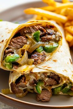 a steak burrito cut in half on a plate with fries