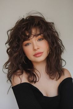 Embrace the autumn season with this chic Fall haircut, showcasing effortless waves and delicate fringed bangs. The subtle volume and natural texture create a laid-back yet sophisticated look, making it perfect for everyday wear. Enhance your style this season with this low-maintenance yet stylish cut. Shaggy Haircut With Fringe, Wavy Haircuts For Volume, Curly Hair Bangs Medium Length, Layered Curly Hair With Fringe, Perm With Fringe, 70s Shag Wavy Hair, Cool Wavy Haircuts, Low Maintenance Haircut Wavy Hair, Loose Waves With Bangs