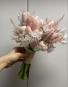 a hand holding a bouquet of flowers in front of a gray wall with white and pink flowers