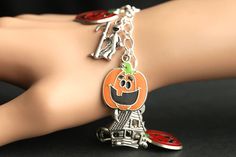 A collection of silver plated Halloween themed charms combined with five enameled Jack o'Lantern charms have been dispersed around a shimmering silver plated bracelet chain in this handmade charm bracelet. This Halloween charm bracelet is then completed with a lobster clasp and a 1/2 inch of chain at the end for adjustable sizing. Charms in this bracelet include five enameled jack o' lantern charms, haunted house charm, grim reaper charm, masquerade mask charm, and screaming skull charm. I also Novelty Silver Halloween Bracelet, Halloween Themed Silver Bracelet, Silver Halloween Novelty Bracelet, Novelty Silver Bracelet For Halloween, Silver Themed Bracelet For Halloween, Halloween Novelty Jewelry With Charms, Halloween Novelty Jewelry Bracelet, Halloween Bracelet Jewelry Gift, Halloween Novelty Bracelet