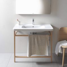 a white sink sitting under a bathroom mirror next to a wooden chair with a towel on it