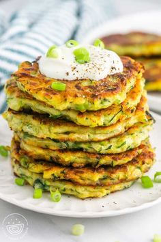 a stack of zucchini fritters on a plate with sour cream and green onions