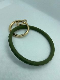 a green ring with two gold rings hanging from it's side on a white surface