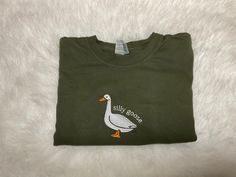 Silly Goose Comfort Colors Shirt, Embroidered Goose Crewneck T-Shirt, Silly Goose Shirt, Embroidered Comfort Colors Shirt, Funny Goose Shirt This embroidered silly goose shirt is everything. Perfect to tell everyone you're a silly goose!   These are embroidered comfort colors shirts they are so comfy and we use high quality thread on all our embroidery items.  ✨ 100% Cotton ✨ Pre-shrunk ✨ Relaxed fit Care: Machine wash: warm  Tumble dry: low Do not iron directly on the print Please message me if Casual Long Sleeve Shirt With Embroidered Logo, Casual Short Sleeve Shirt With Letter Embroidery, Casual Short Sleeve Shirt With Custom Embroidery, Casual Long Sleeve Shirt With Embroidered Graphics, Fall Embroidered Crew Neck Shirt, Embroidered Crew Neck Shirt For Fall, Fall Short Sleeve T-shirt With Embroidered Logo, Green Long Sleeve T-shirt With Custom Embroidery, Casual Long Sleeve Shirt With Custom Embroidery