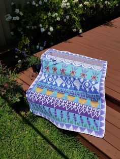 a blue and white blanket sitting on top of a wooden deck next to flowers in a garden