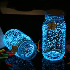 two mason jars filled with blue lights on top of a black table next to colored crayons