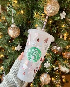 someone holding up a starbucks cup in front of a christmas tree with ornaments on it