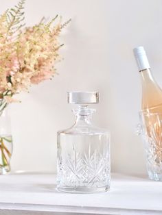 a glass bottle sitting on top of a table next to a vase filled with flowers