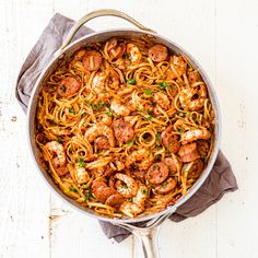 a skillet filled with shrimp and pasta on top of a wooden table next to a napkin