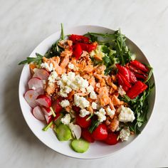 a white bowl filled with lots of food on top of a marble countertop next to sliced radishes and cucumbers