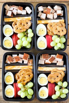 four black trays filled with food on top of a wooden table next to each other