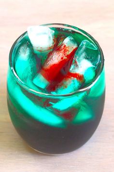 a green drink with ice cubes in it sitting on a wooden table next to a red and white object