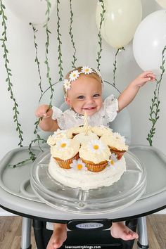 a baby sitting in a highchair with cupcakes and balloons