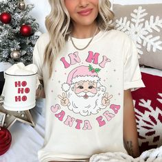 Step into the whimsical world of Santa Claus with our "In My Santa Era Funny Shirt." This shirt is a comical nod to a time when Santa was the ultimate trendsetter, blending the magic of the North Pole with some hilarious yuletide humor. Comfort Colors introduces its garment-dyed t-shirt; a fully customizable tee made 100% with ring-spun cotton. The soft-washed, garment-dyed fabric brings extra coziness to your wardrobe while the relaxed fit makes it an excellent daily choice. The double-needle s Cotton Top With Character Print For Holidays, Holiday Cotton Tops With Character Print, Casual Holiday Tops With Character Print, Casual Character Print Tops For Holiday, Cute Letter Print T-shirt For Holiday, Holiday Cotton Top With Character Print, Casual Character Print Holiday Tops, Fun Cartoon Print Tops As Gift, White Tops With Cartoon Print For Christmas