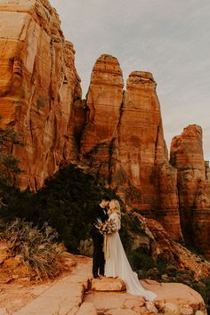 a bride and groom standing on top of a rock formation in front of some mountains