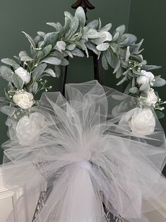 a wreath with white flowers and greenery hanging from the top of a metal chair