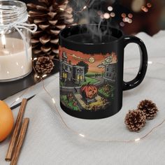 a black coffee mug sitting on top of a table next to an orange and pine cone