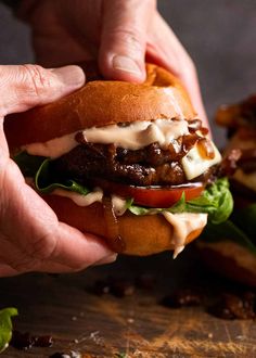 two hands holding a sandwich with meat, cheese and lettuce on it next to other food items