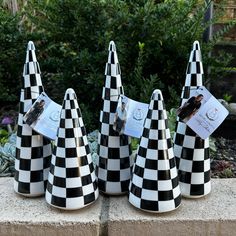 three black and white checkered cone shaped vases with tags on them sitting in front of some bushes