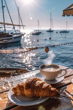 coffee and croissants sit on a table overlooking the water