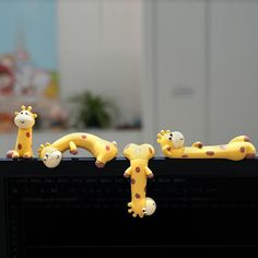 three toy giraffes are sitting on top of a computer monitor, one is yellow and the other is brown