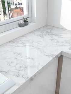 a white marble counter top next to a window with a potted plant on it