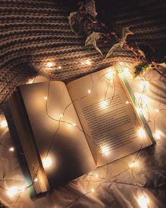 an open book sitting on top of a bed covered in lights