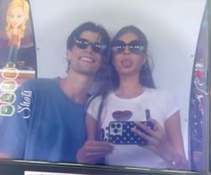 a man and woman taking a selfie in front of a television screen with their cell phone