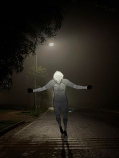 a person walking down a street at night with their arms out in the air and lights on